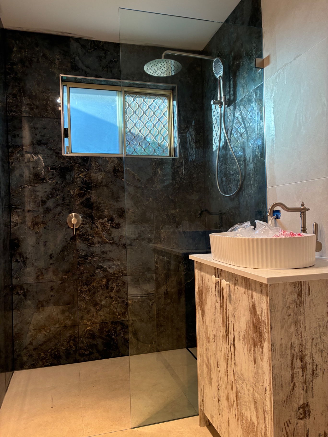 Walk-in glass shower panel against dark marble tiles